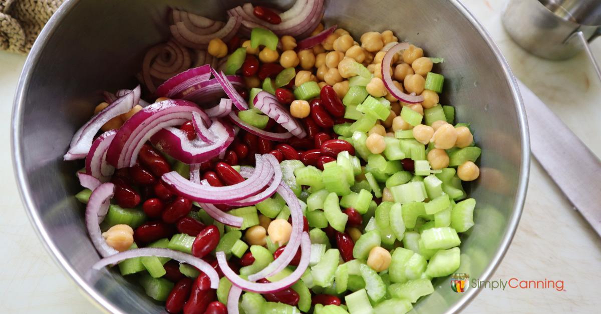 Sliced purple onion, celery, kidney and garbanzo beans in a metal bowl.