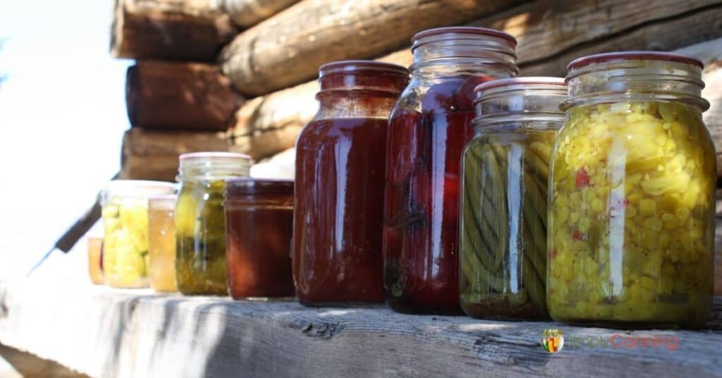 Jars of colorful home canned food lined up on a wooden ledge.