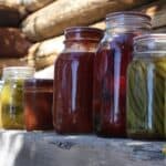 Jars of colorful home canned food lined up on a wooden ledge.