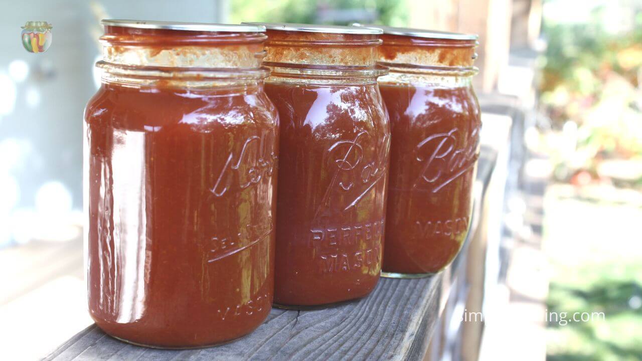 Three pint jars of tomato sauce on a deck railing. 