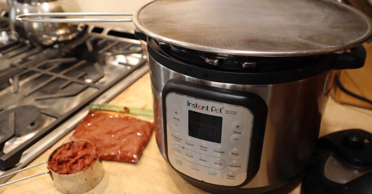 Instant pot on a counter with a cup of tomato paste sitting next to it.