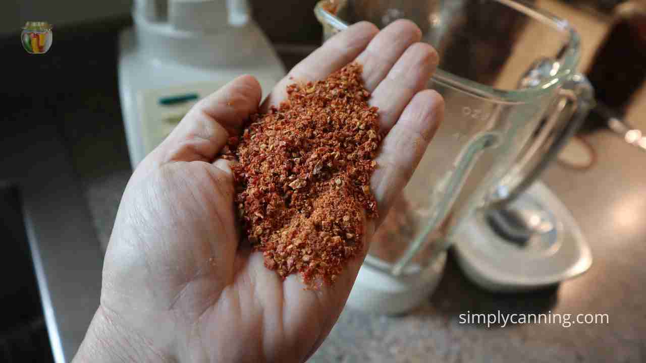 A hand delicately holds a small amount of tomato powder, showcasing its rich color and texture.