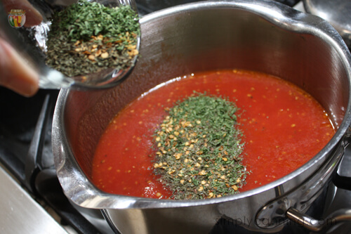 Adding dried seasonings to a pot of tomato sauce. 