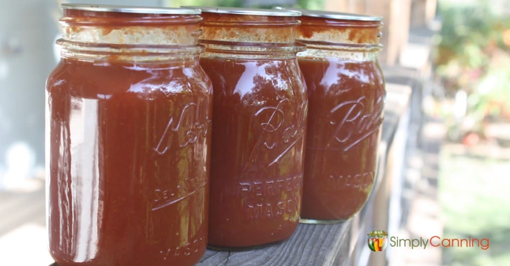 Three canning jars with tomato sauce lined up next to each other outdoors.