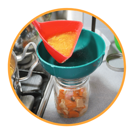 Pouring soup into a canning jar through a green canning funnel.