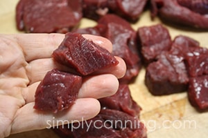 Holding a few cubes of freshly cut venison with more venison pieces on a cutting board below.