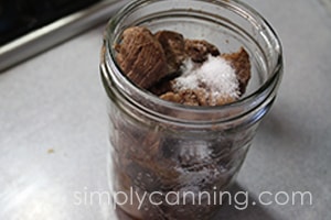 Sprinkling salt into a jar packed with cooked venison pieces.
