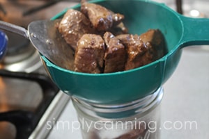 Spooning pieces of meat into a canning jar.