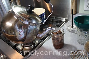 Pouring hot liquid from a teapot into a jar of venison chunks.