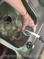 Rinsing canning jars in the sink under running water.
