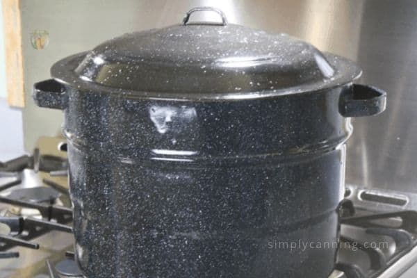 Black graniteware water bath canner sitting on the stovetop.