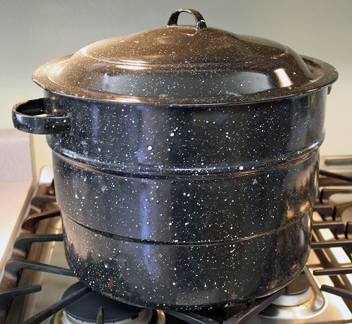Black speckled graniteware waterbath canner sitting on the stovetop.