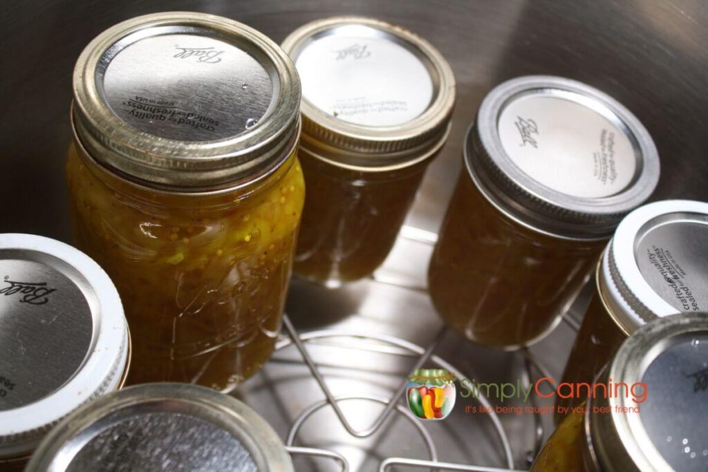 Close up of pint and half pint jars of zucchini relish in a stainless steel waterbath canner.